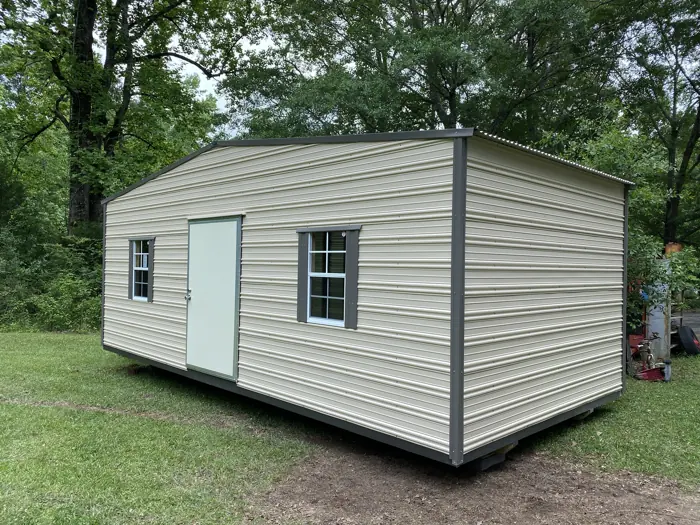 Cream aluminum shed with dark grey trim and shutters in a shaded yard