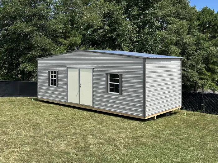 Light grey aluminum shed with double doors and two shuttered windows in a backyard