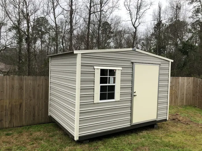 Grey aluminum shed with cream trim and a single door in a fenced backyard