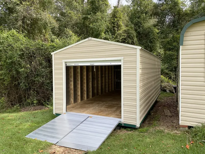 Cream aluminum shed with the roll-up door open, showing the framed interior and floor, with a wide aluminum ramp