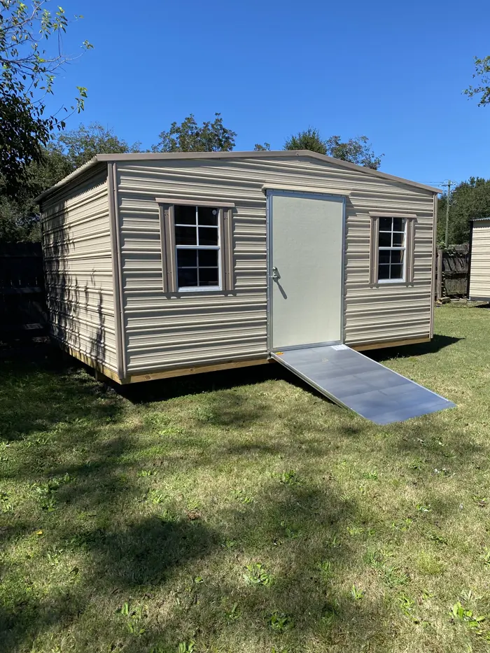 Tan aluminum shed with matching shutters, a single door and an aluminum ramp in a sunny yard