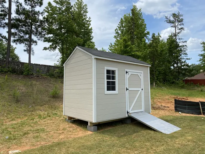 Beige wood shed with lap siding leveled on concrete blocks with an aluminum ramp