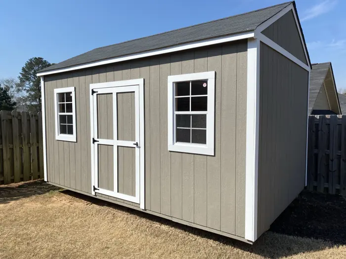 Grey wood shed with white trim, a single door and two windows in a backyard