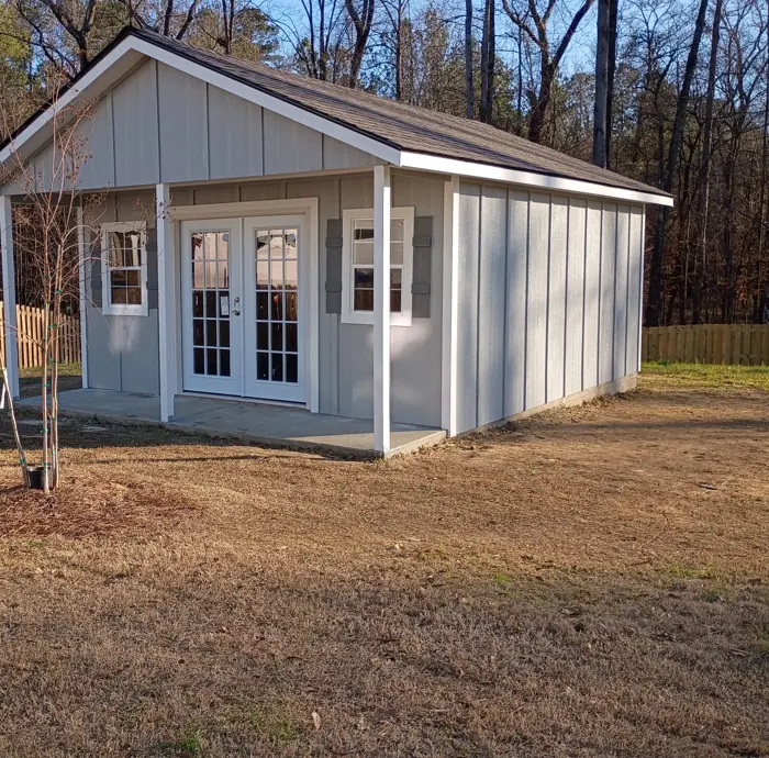 Grey wood building with a covered front porch, French doors and shutters