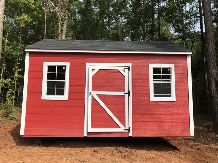 Red wood shed with lap siding, white trim and two windows, built among pine trees