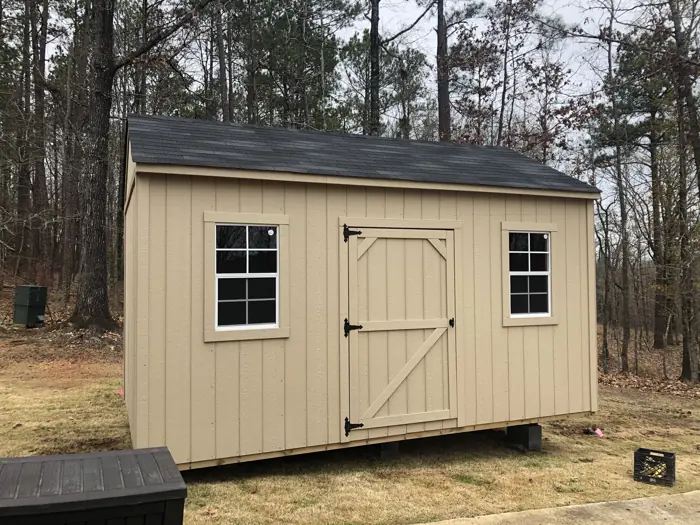 Tan wood shed leveled on concrete blocks on a sloped wooded lot